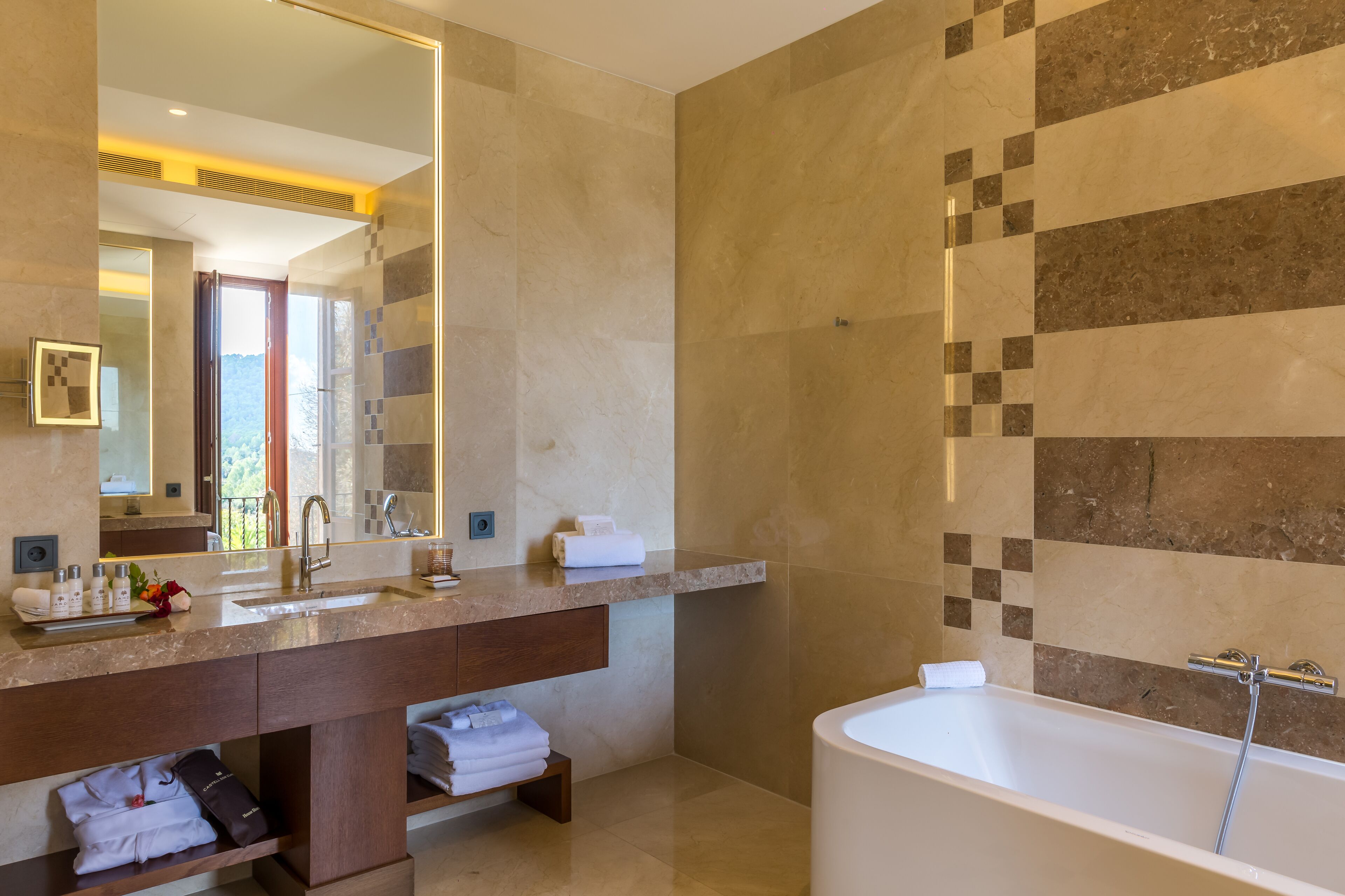 Un baño moderno con un espejo grande, una bañera y un tocador con artículos de aseo.