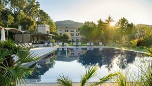 A swimming pool with lounge chairs, a covered seating area, and a building with a turret in the background.