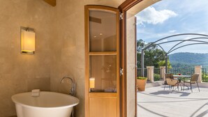 A bathroom with a freestanding bathtub, a glass-enclosed shower, and a view of a patio with outdoor seating.