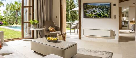 Una sala de estar moderna con un ventanal grande, un sofá cómodo, una mesa de centro con fruta y vistas a una piscina y jardín.
