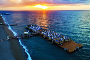 A pier extending into the ocean with rows of blue lounge chairs and umbrellas, a wooden deck, and a view of the sunset over the water.