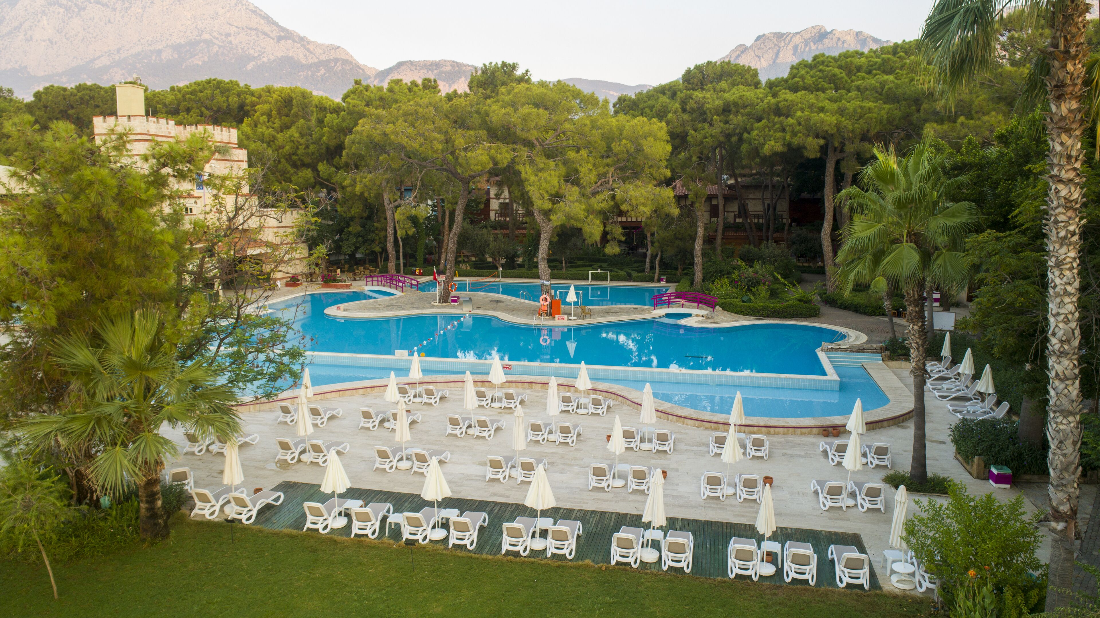 A swimming pool with lounge chairs and umbrellas, surrounded by trees and buildings.