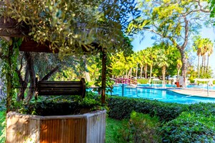 Zona de piscina con un banco de madera, rodeada de vegetación exuberante y palmeras.