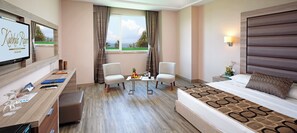 Ein Hotelzimmer mit einem Bett, zwei Sessel, einem Schreibtisch mit Computer, einem Fernseher und einem Fenster mit Blick.