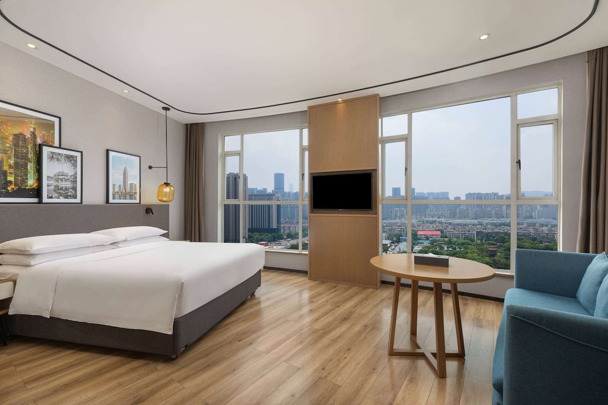 A modern hotel room with a large bed, a TV, a small table, and a city view.