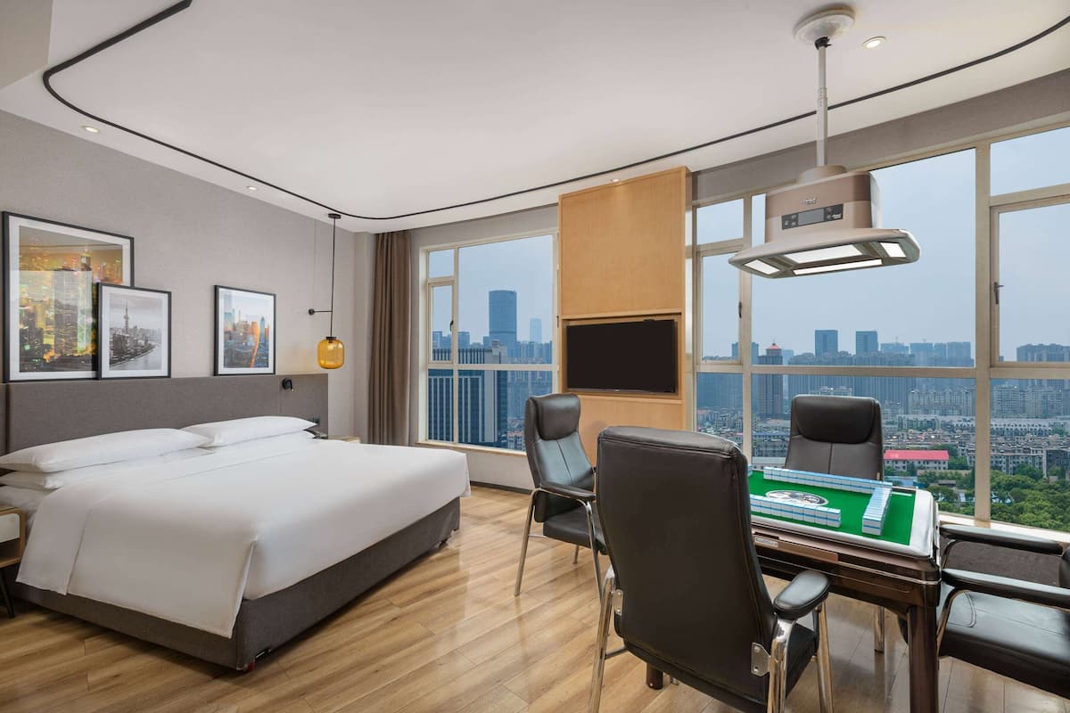 A hotel room with a bed, a desk with a green board game, a chair, and a TV.