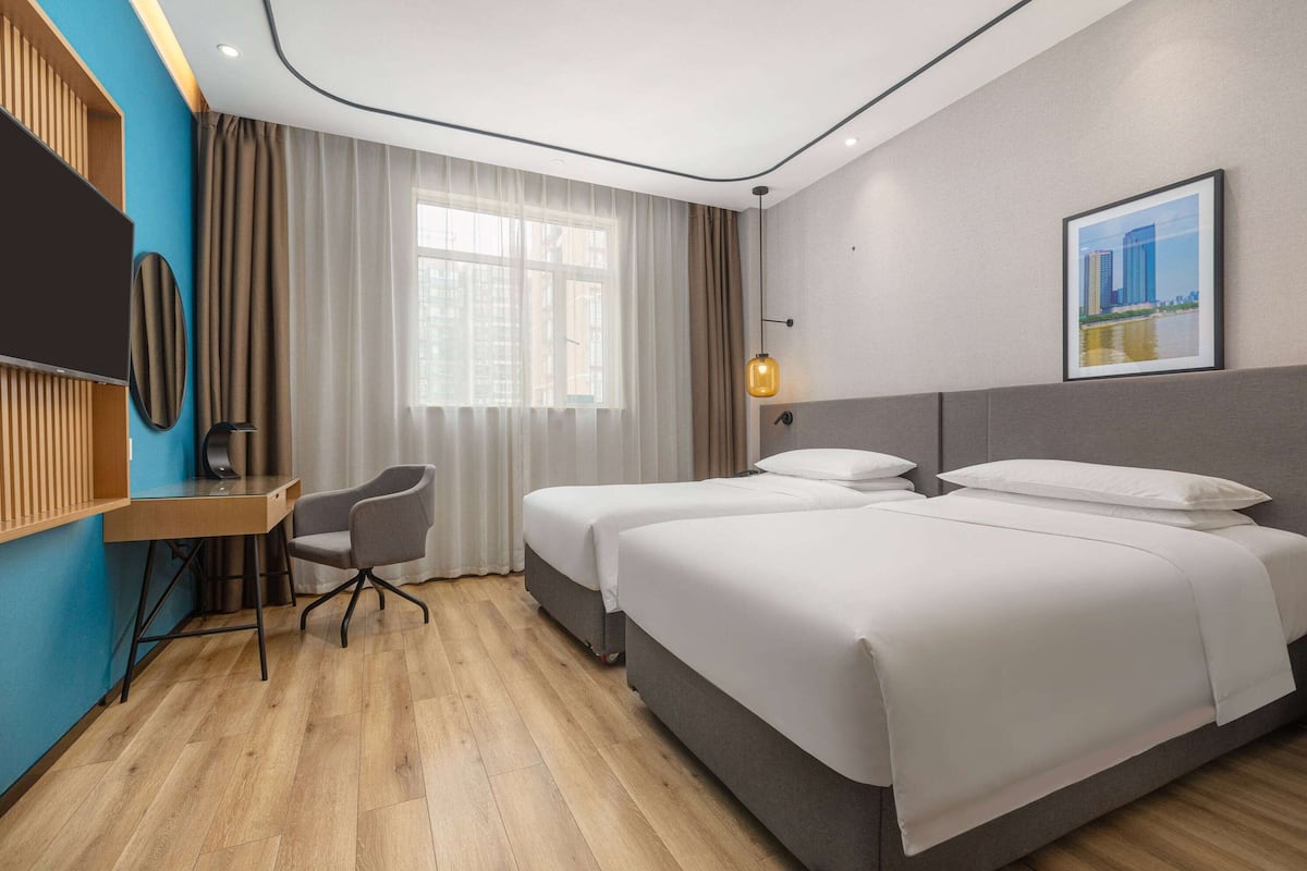 A hotel room with two beds, a desk, a chair, a TV, and a window with curtains.