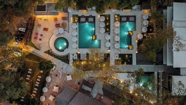 Eine Vogelperspektive zeigt ein Resort mit mehreren Schwimmbecken, Liegestühlen und Sitzbereichen im Freien.