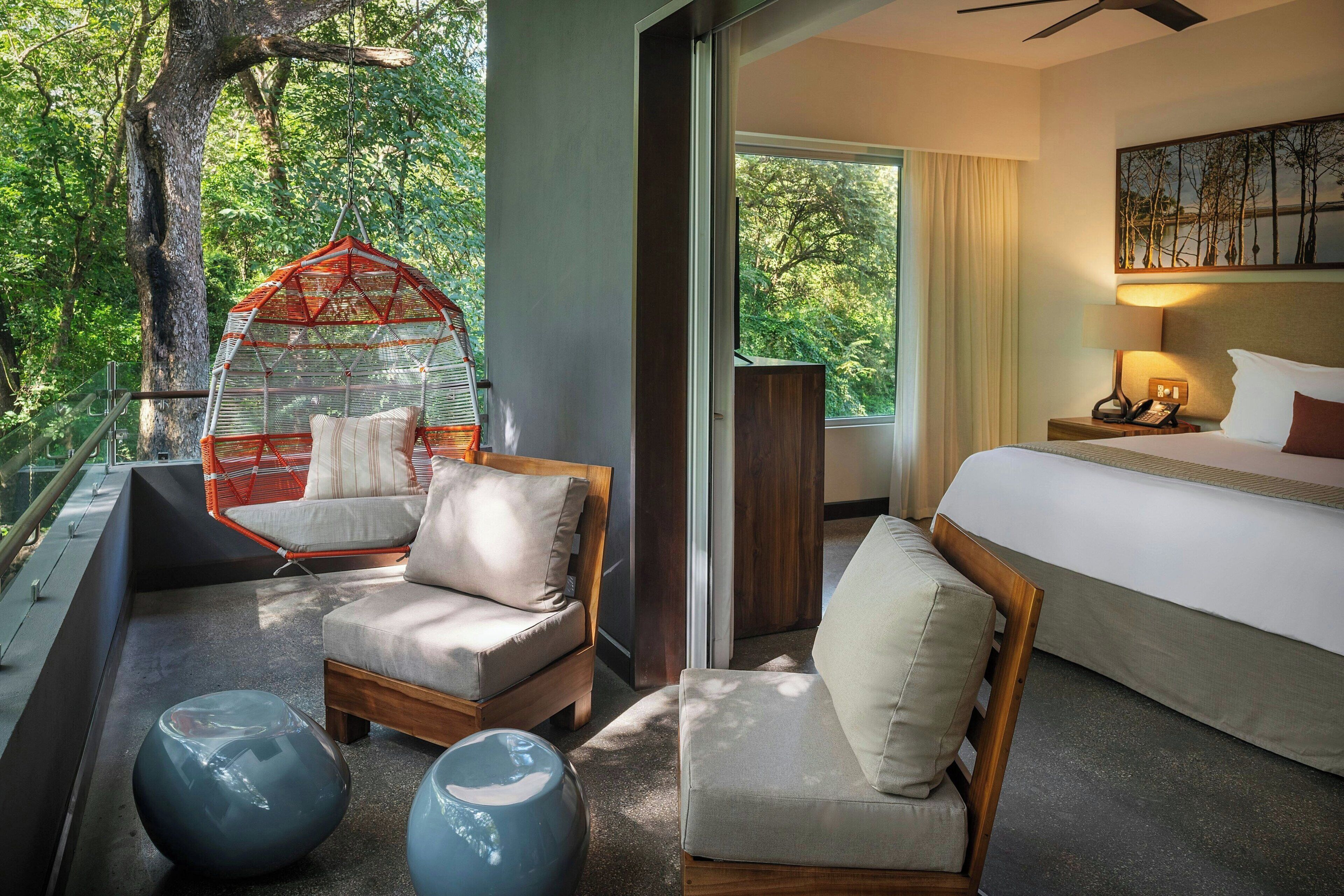 Een moderne hotelkamer met een groot bed, twee zithoeken, een hangstoel en uitzicht op het omliggende landschap.