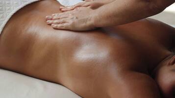 A massage therapy session in a spa setting with a massage table, a small table with bottles, and a window with sunlight.
