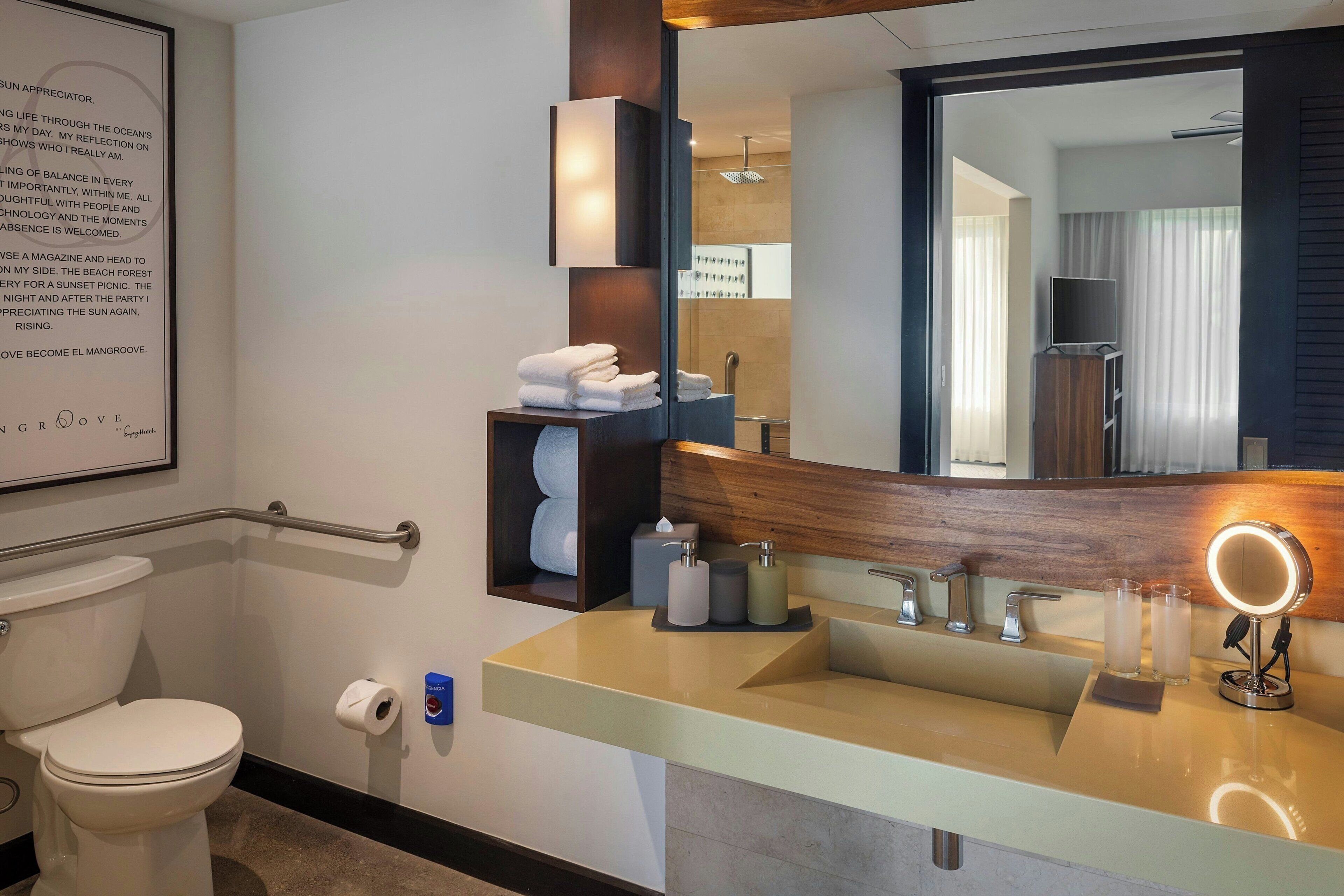 Une salle de bain moderne avec un grand miroir, un lavabo avec un meuble-vasque, des toilettes et un espace douche visible à travers la porte en verre.