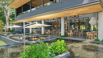 An outdoor dining area with tables and umbrellas, surrounded by a water feature and greenery.