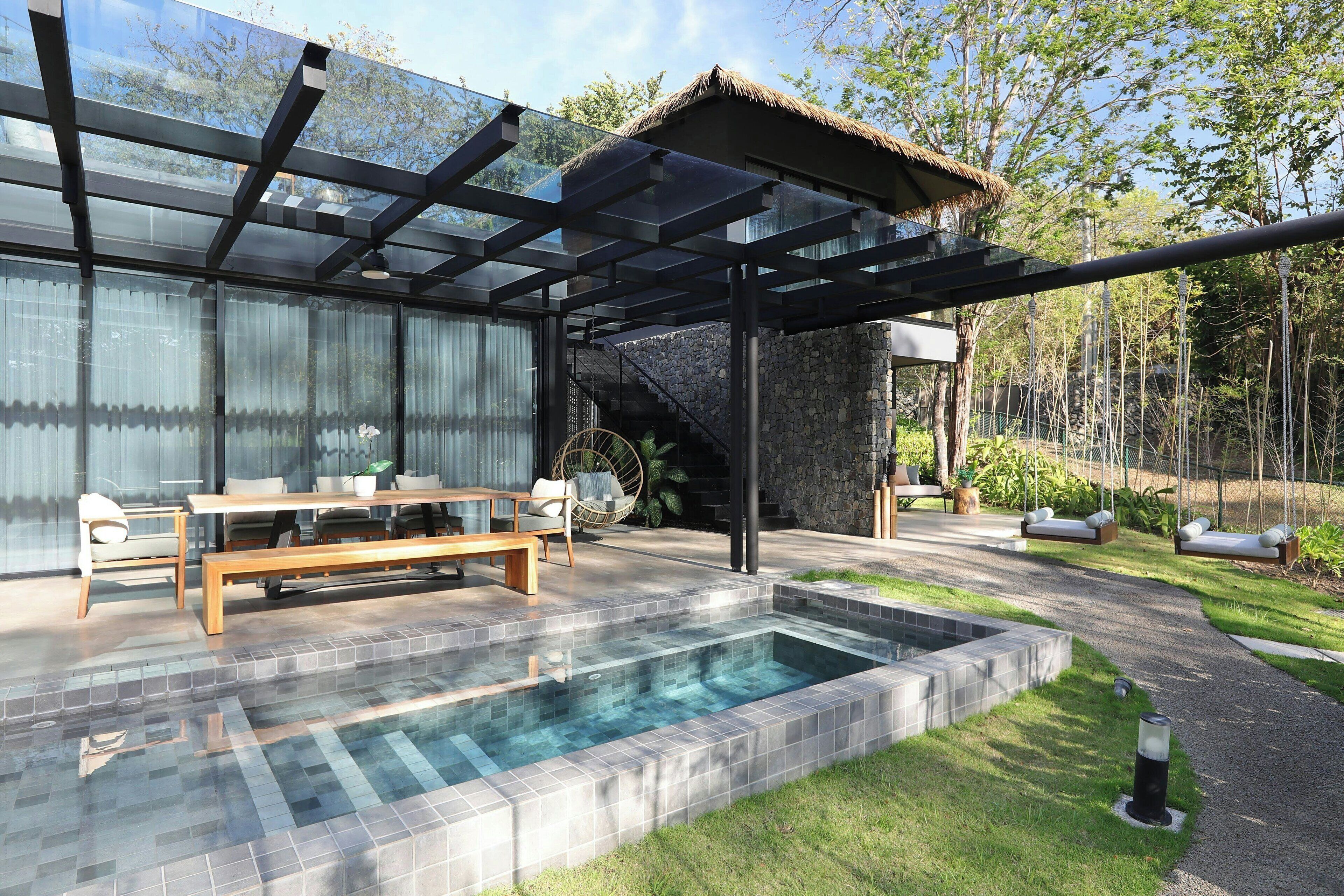 Un espace piscine extérieur moderne, doté d’une structure en verre, d’un banc en bois et d’une structure en pierre.