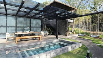 Area piscina esterna moderna con recinto in vetro, una panca in legno e una struttura in pietra.