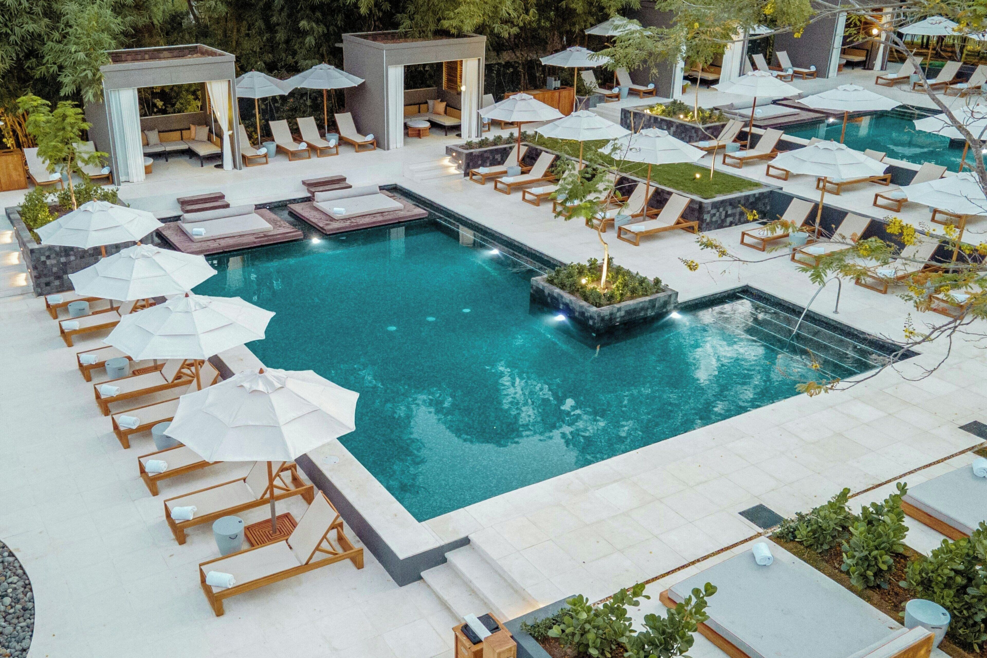 Un espace piscine aménagé avec des chaises longues, des parasols et une petite cascade décorative.