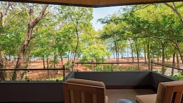 Un balcon avec vue sur une forêt et une plage. On y trouve deux chaises et une petite table.
