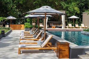 Un área junto a la piscina con sillones de madera, sombrillas y un mueble de madera.