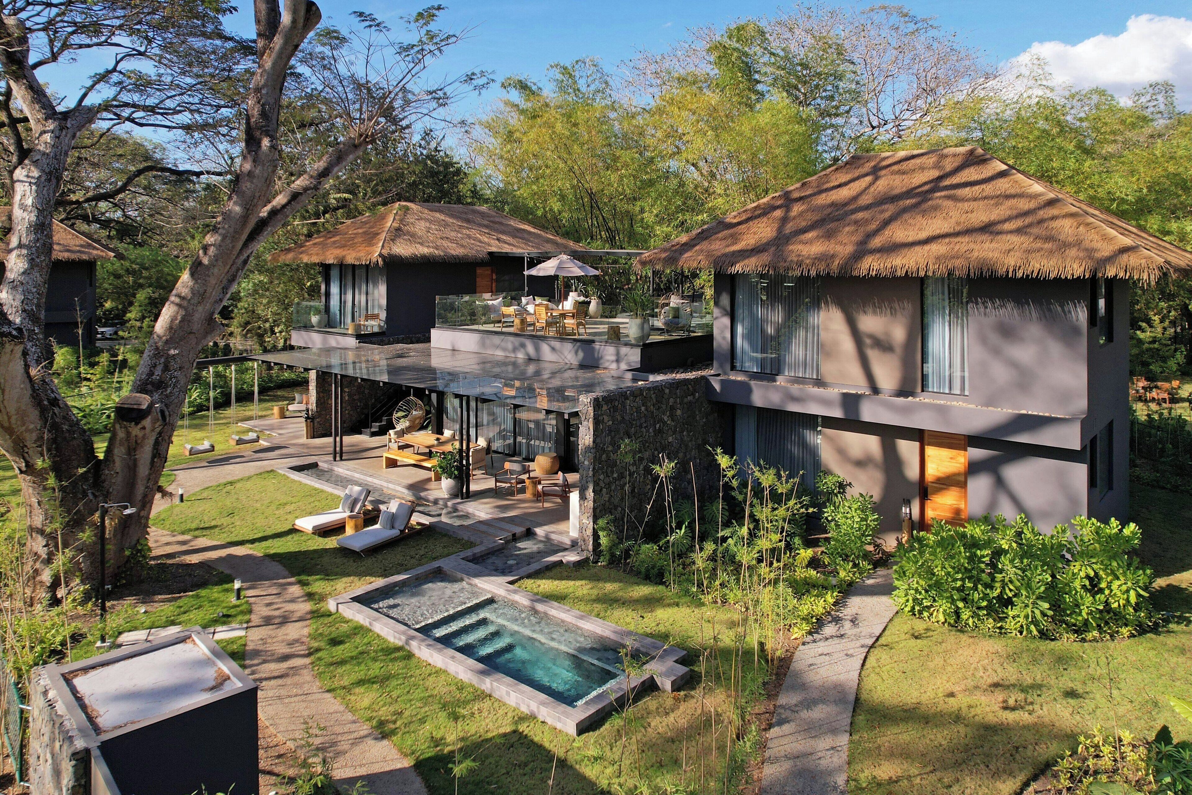 Una villa moderna con piscina, mobiliario exterior y una estructura de techo de paja.