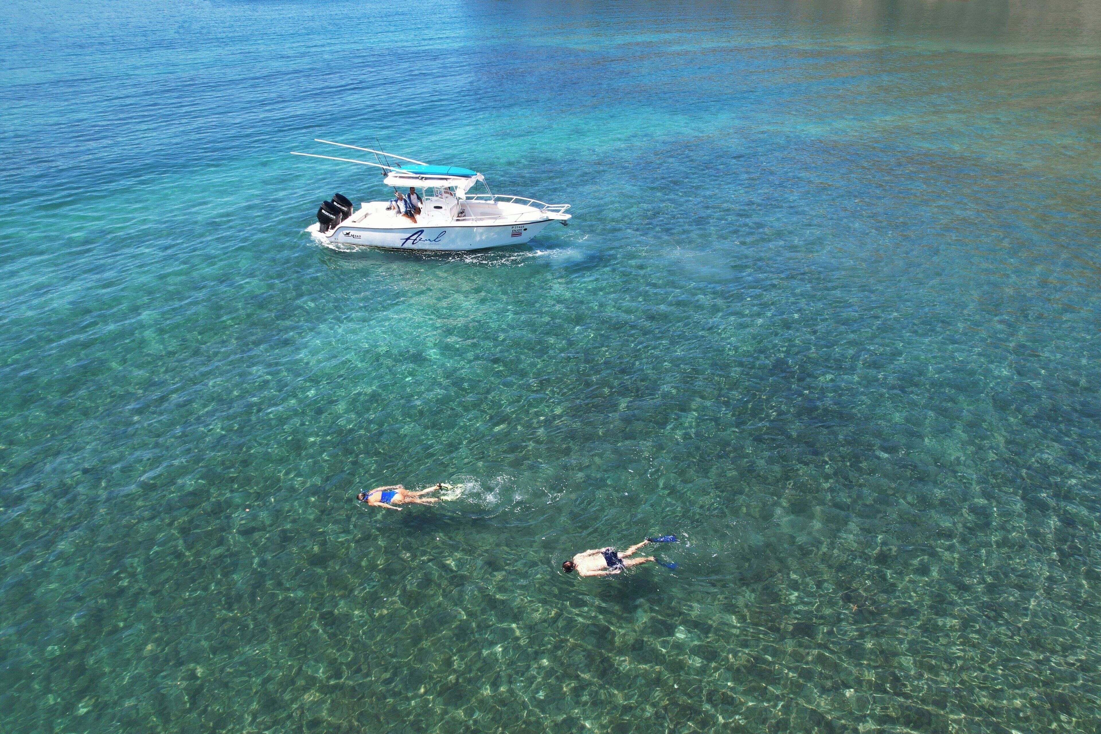 A boat with two people swimming nearby.