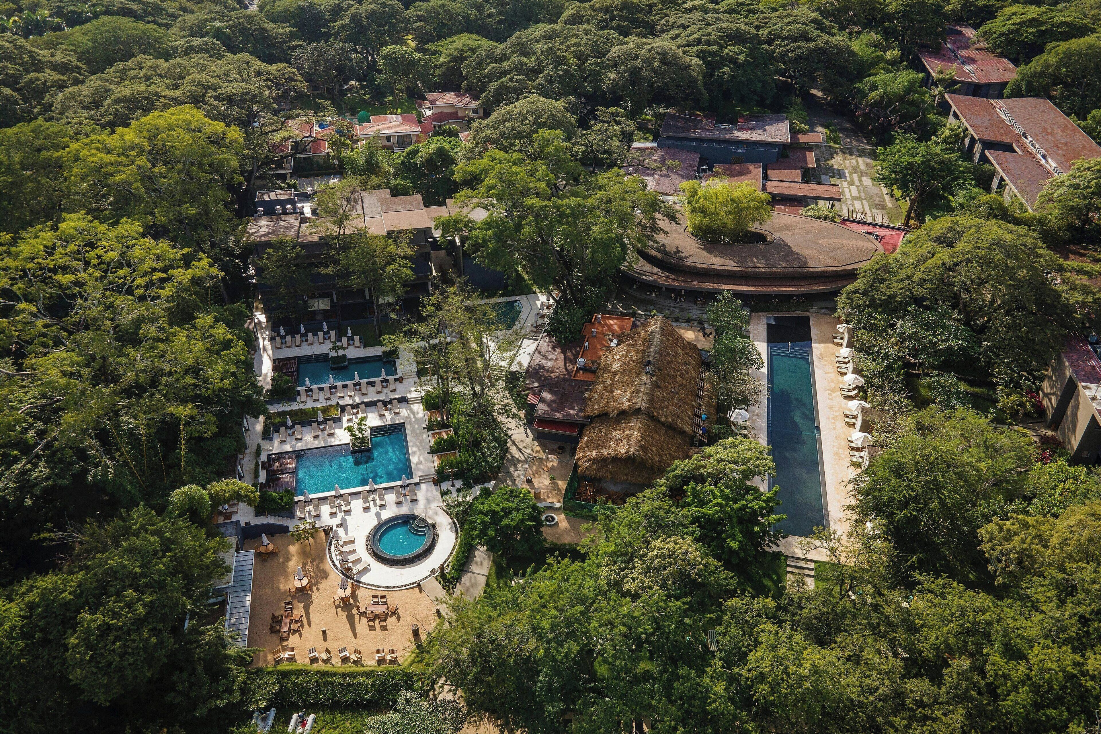Une vue aérienne d’un complexe hôtelier doté de plusieurs piscines, d’une végétation luxuriante et de différents bâtiments.