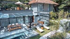 Ein modernes Haus mit einer glasüberdachten Terrasse, einem Whirlpool und einem Essbereich mit Gartenmöbeln.