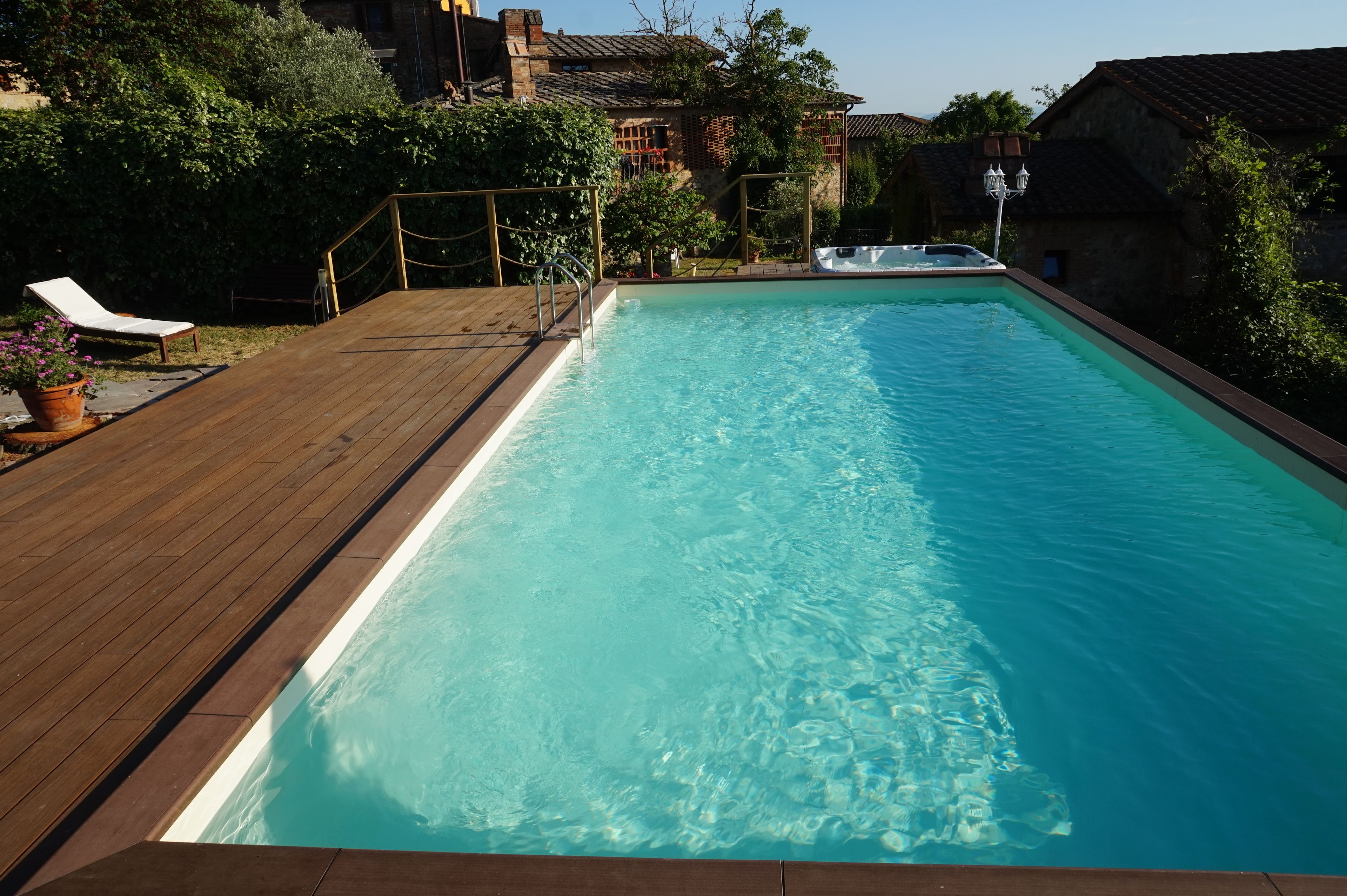 A rectangular swimming pool with a wooden deck and a hot tub.