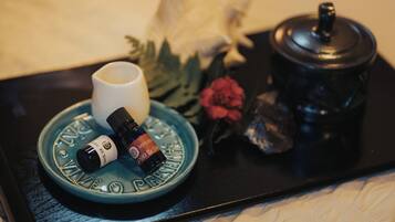 Un plateau avec une assiette bleue, une tasse blanche, un flacon d’huile essentielle, un récipient noir avec un couvercle et quelques fleurs.