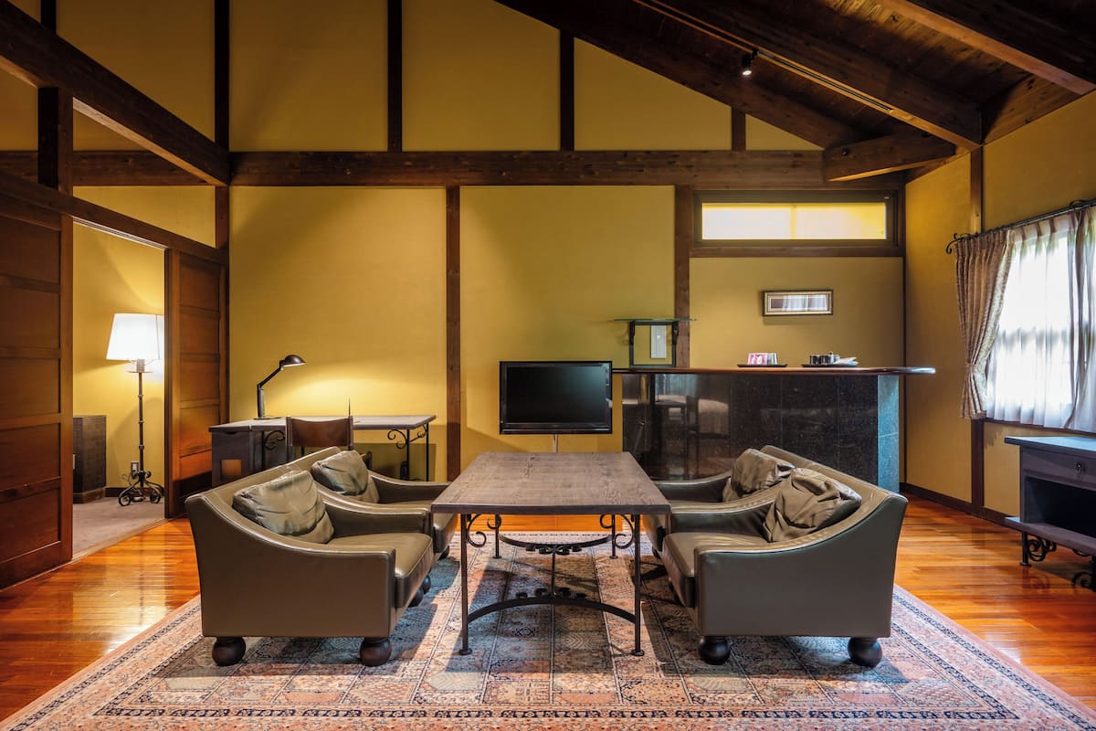 Una sala de estar acogedora con techo de madera, una mesa grande, dos sofás, un televisor y una chimenea.