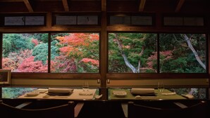 A dining area with a view of autumn foliage through large windows.