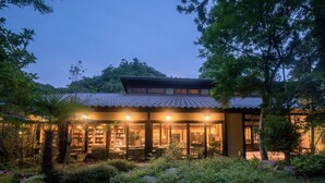 A traditional Japanese-style building with a tiled roof, surrounded by lush greenery and a stone pathway leading to the entrance.
