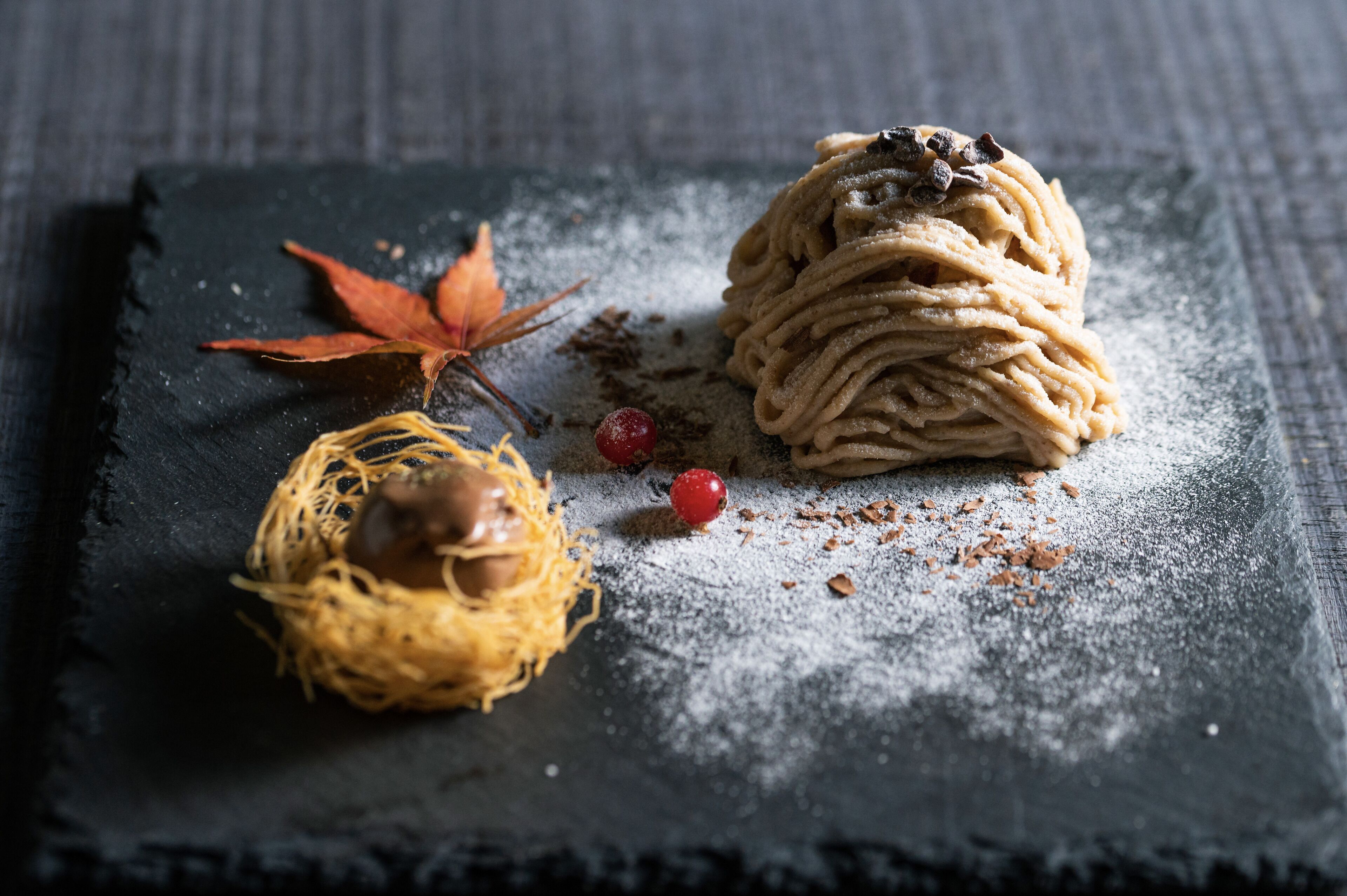 Un dessert à la forme évoquant un nid, surmonté d’une généreuse portion de crème fouettée, le tout présenté sur une surface d’ardoise.
