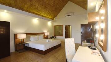A hotel room with a wooden ceiling, a large bed with white linens, a bedside table with a lamp, a chair, a desk with a mirror, and a telephone.