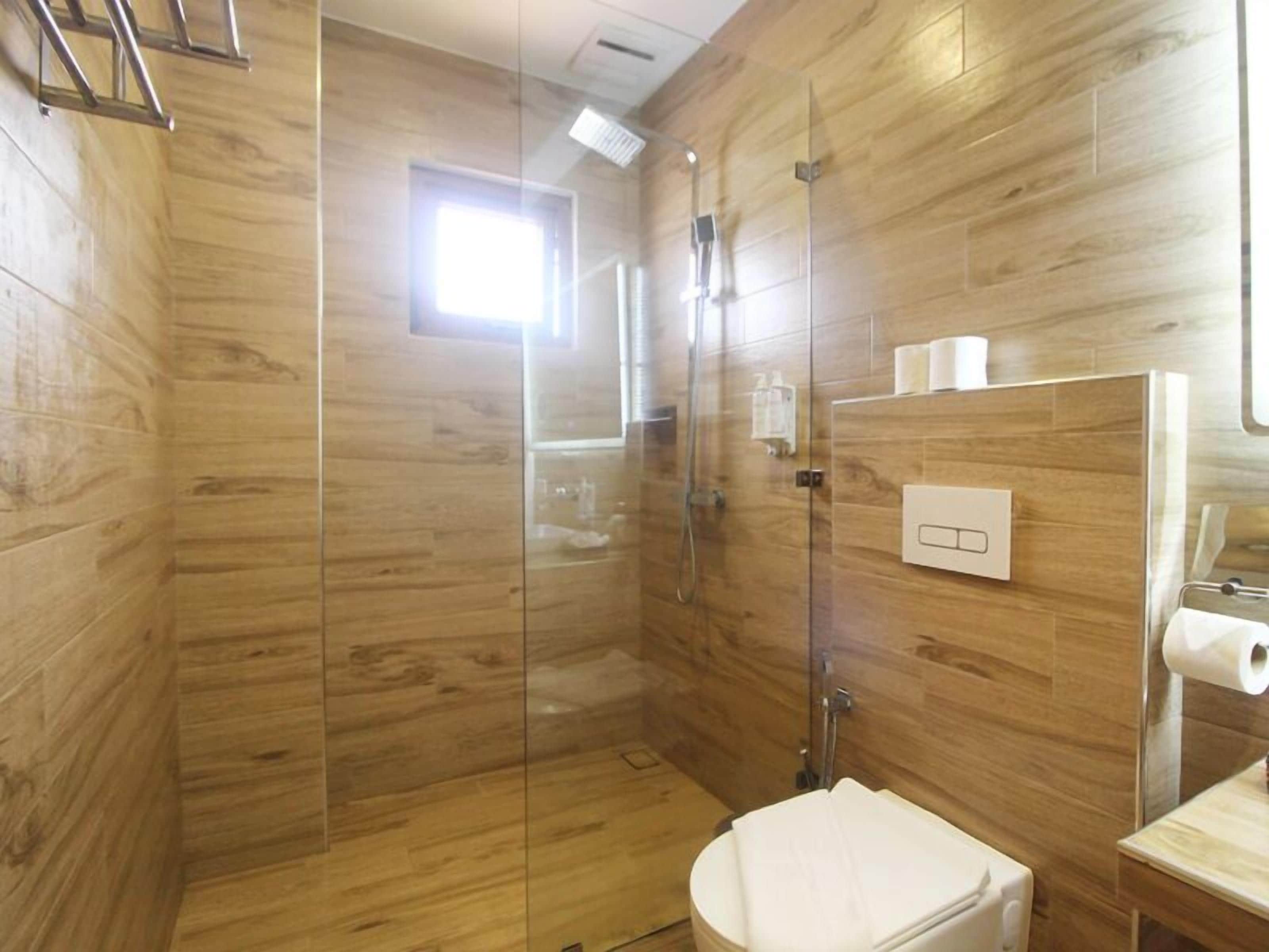 Un baño moderno con paneles de madera, cabina de ducha con mampara de vidrio, inodoro y lavamanos con espejo.