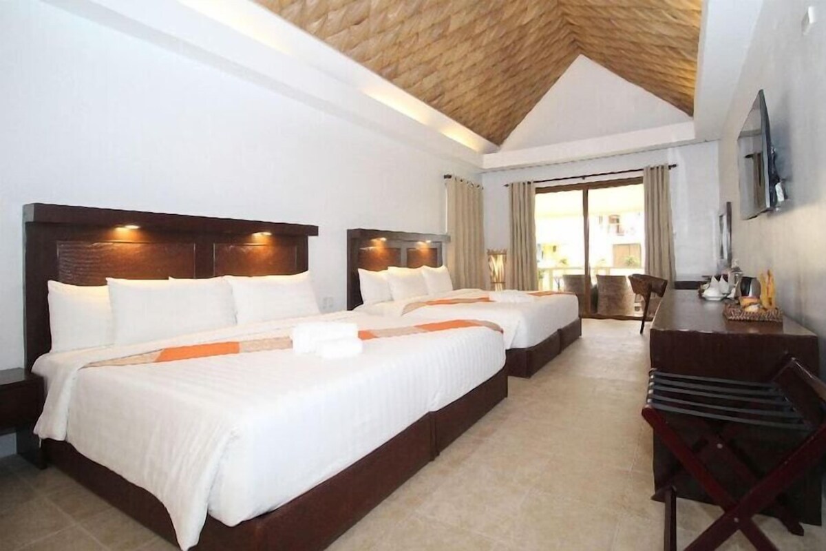 A hotel room with two beds, a wooden ceiling, a desk, and a chair.