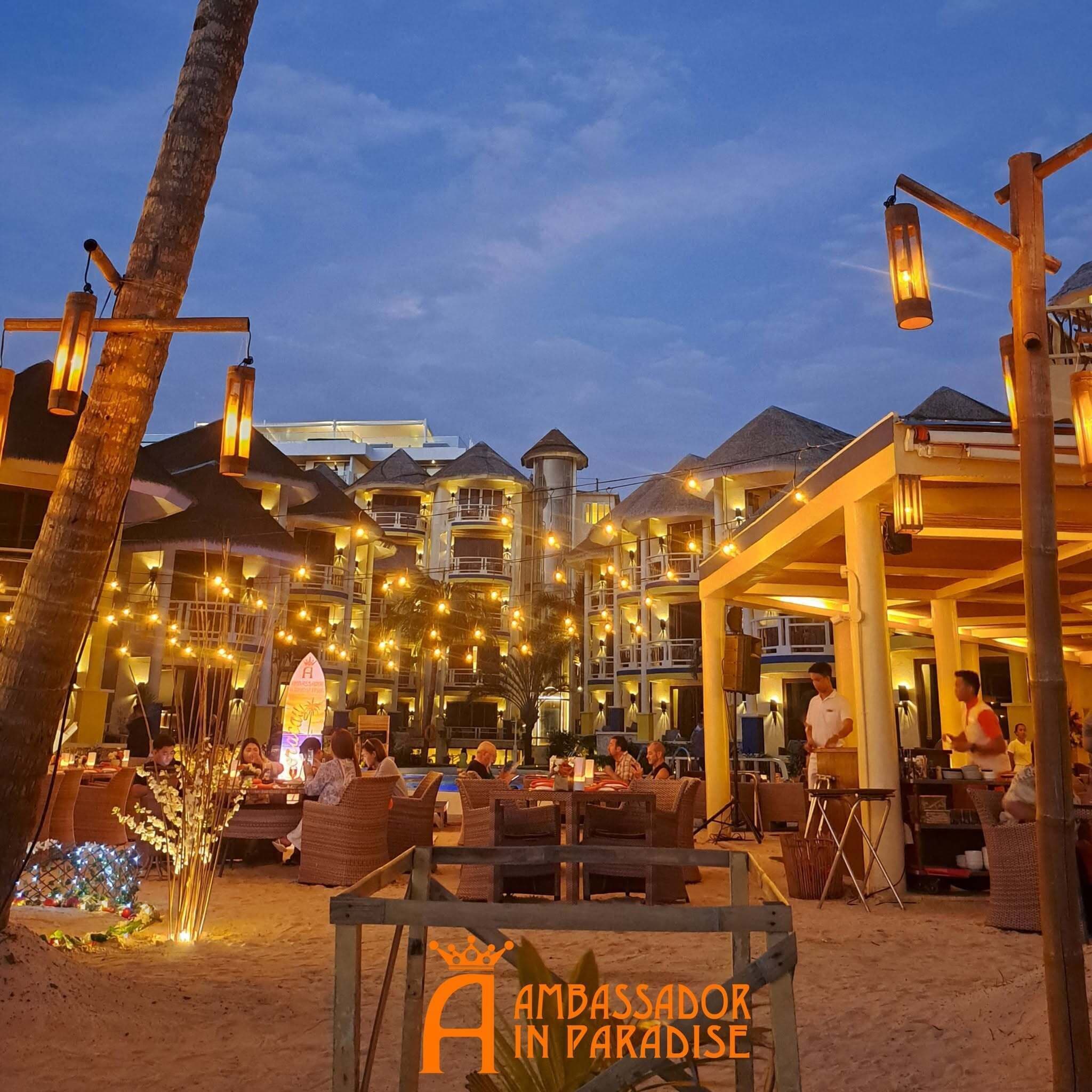 A beachfront resort with outdoor seating and a sign reading 'Ambassador in Paradise'.