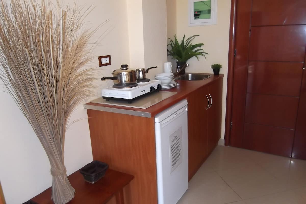 A compact kitchen with a stove, sink, and a small refrigerator. There is a wooden bench and a decorative plant.