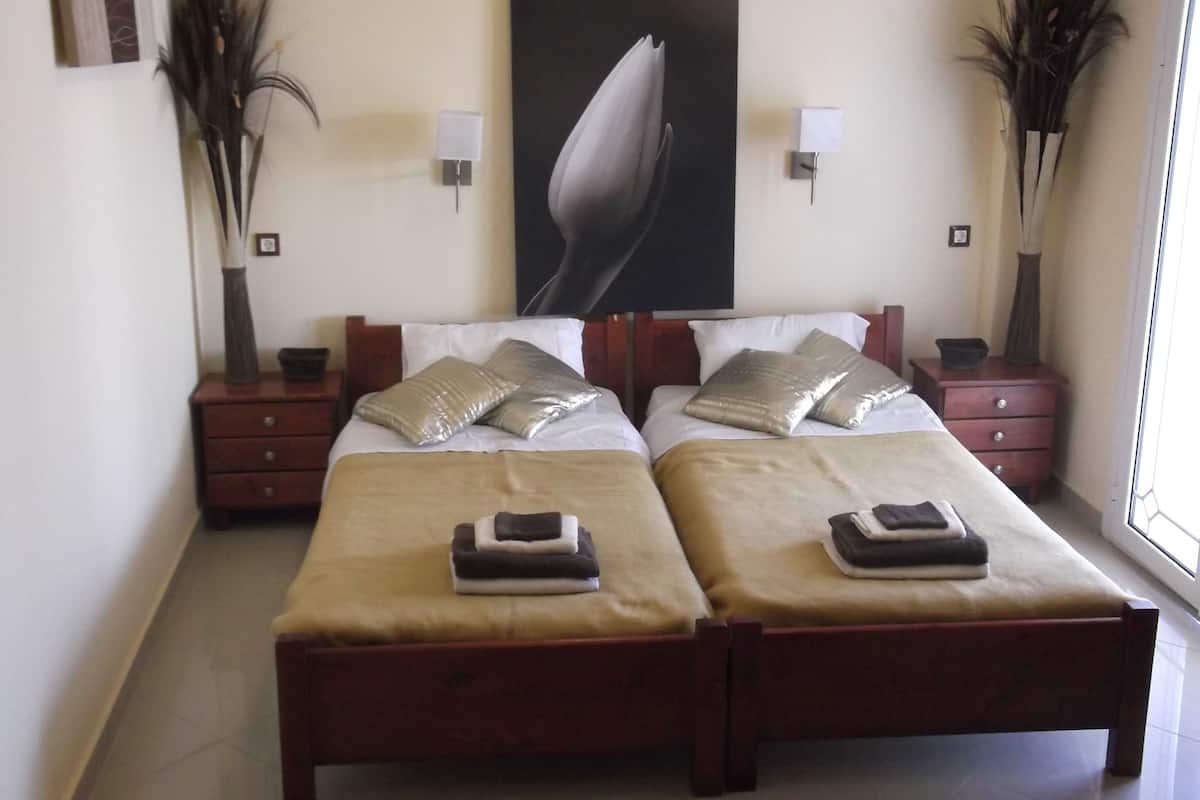 A double bed with two nightstands, a large floral artwork above the bed, and two tall vases on either side.