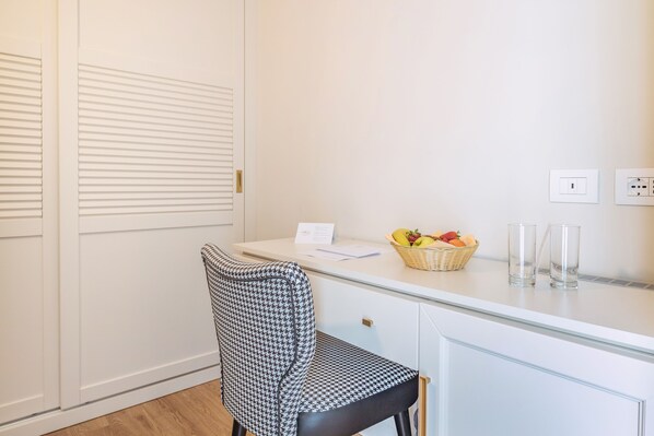 Una habitación con un escritorio blanco, una silla de pata de gallo, una cesta de fruta y dos vasos.