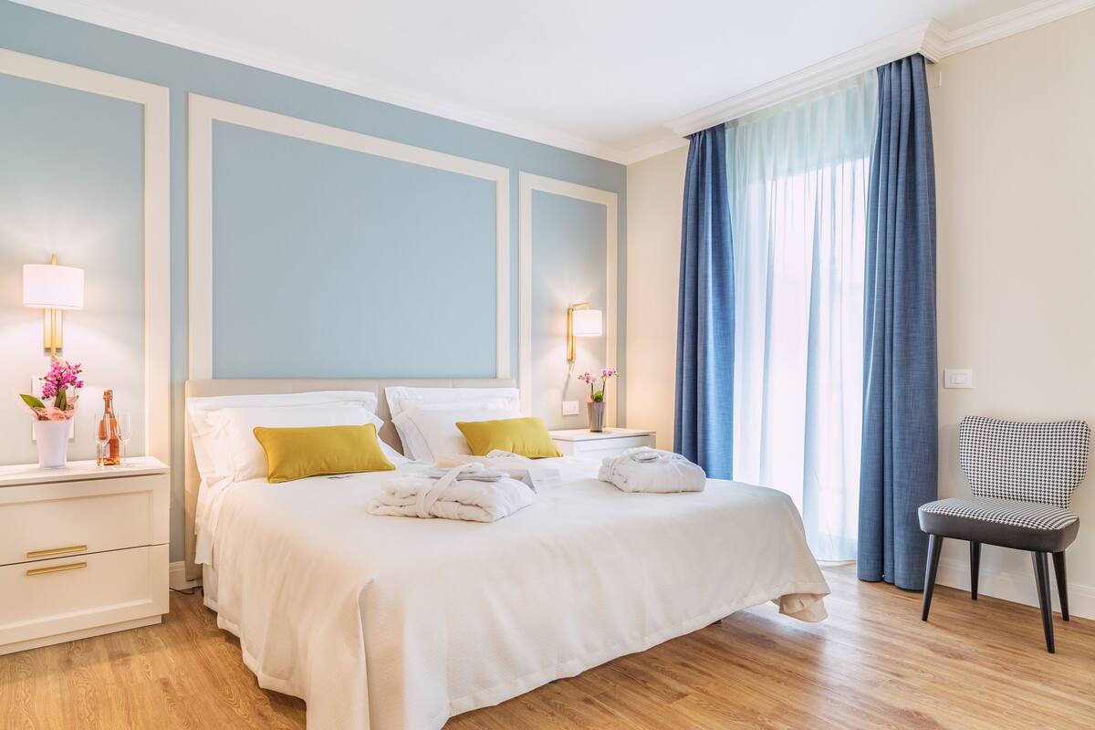A hotel room with a large bed, two bedside tables, a chair, and a window with curtains.