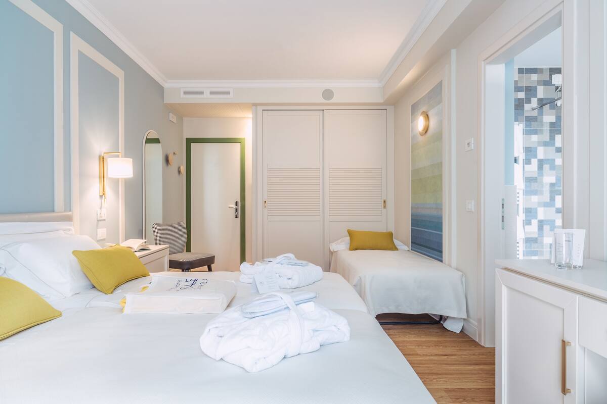 A hotel room with two beds, a desk, a chair, and a bathroom visible through an open door.