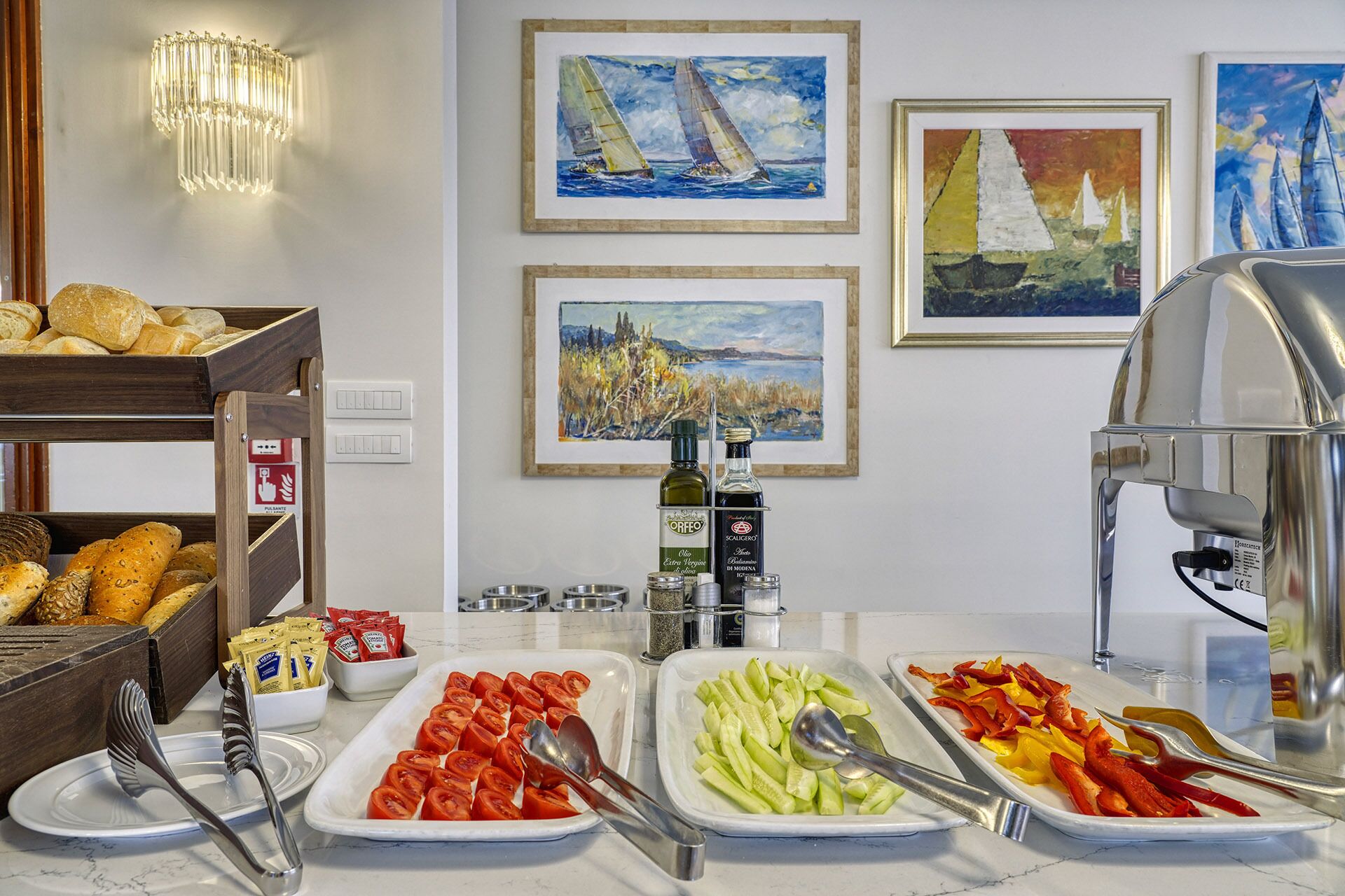 Una mesa de buffet con diversos alimentos y salsas, incluyendo tomates en rodajas, pepinos y pimientos, además de pan y pasteles.