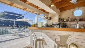 Zona de bar con vistas a las montañas, techo de madera y barra con diversas botellas y vasos.