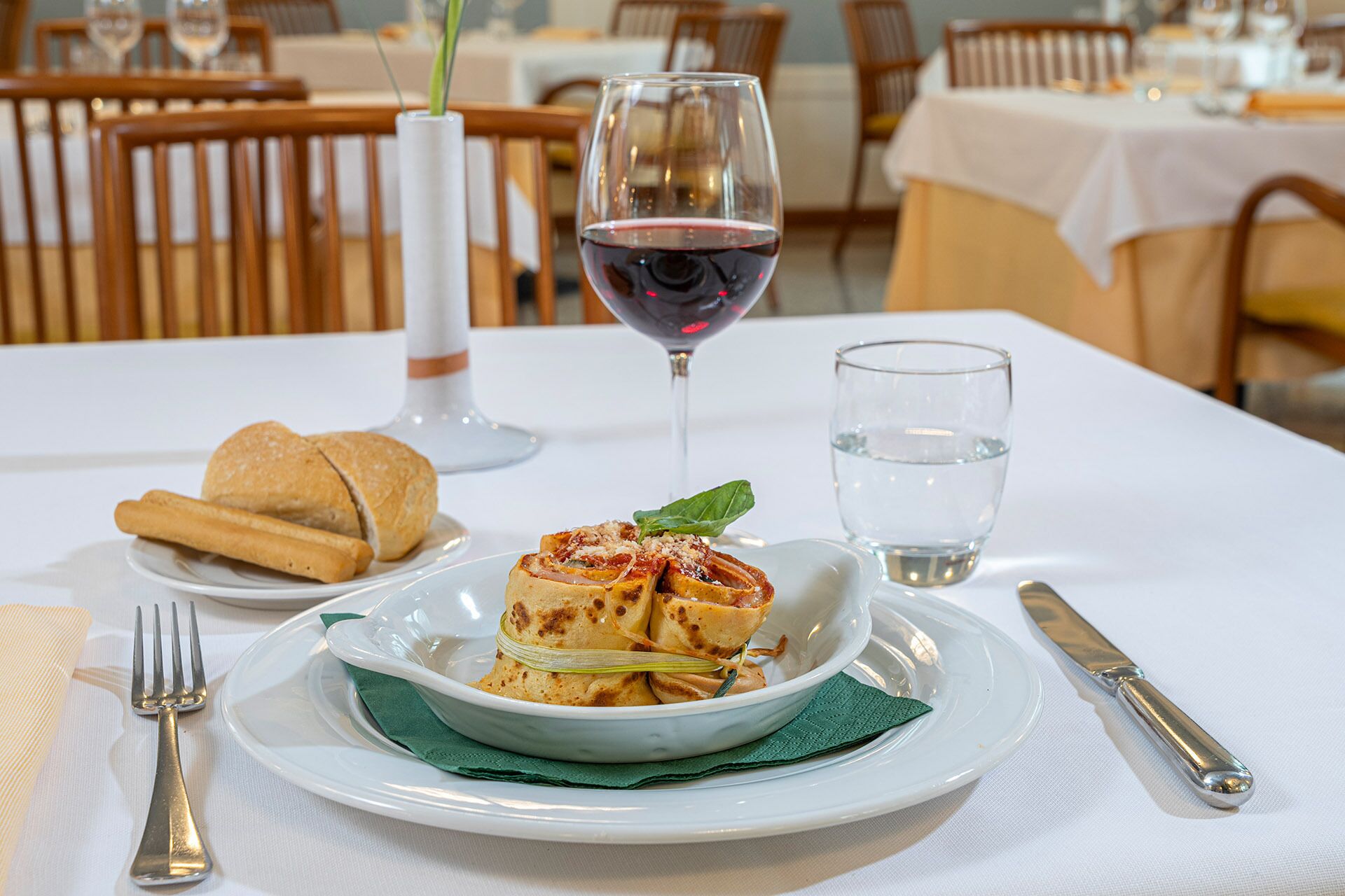Ein Esstisch mit einem Teller Essen, einem Glas Rotwein und einem Glas Wasser.