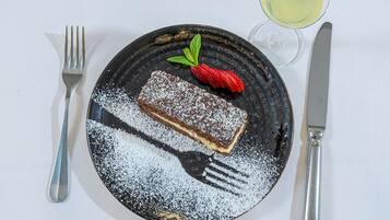 A dessert plate with a piece of cake, a strawberry, and a glass of white wine on a tablecloth.