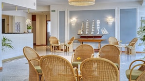 Un hall con sillones de mimbre, un modelo de barco, una araña y un mostrador de recepción.