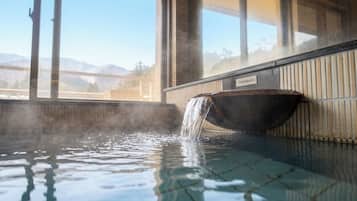 A hot tub with a waterfall feature, a view of mountains through large windows, and a tiled floor.