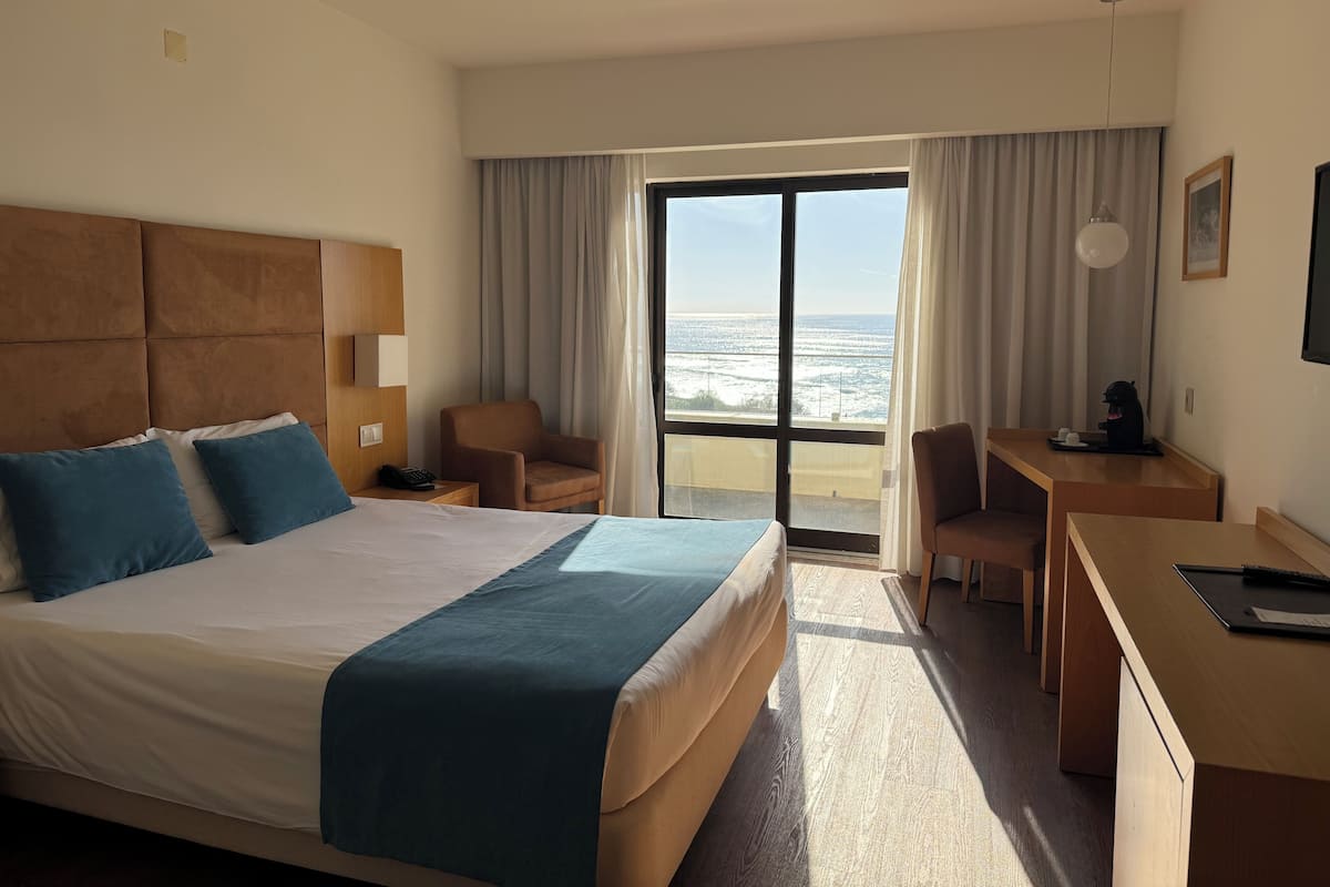 A hotel room with a large bed, a desk, a chair, and a view of the ocean.