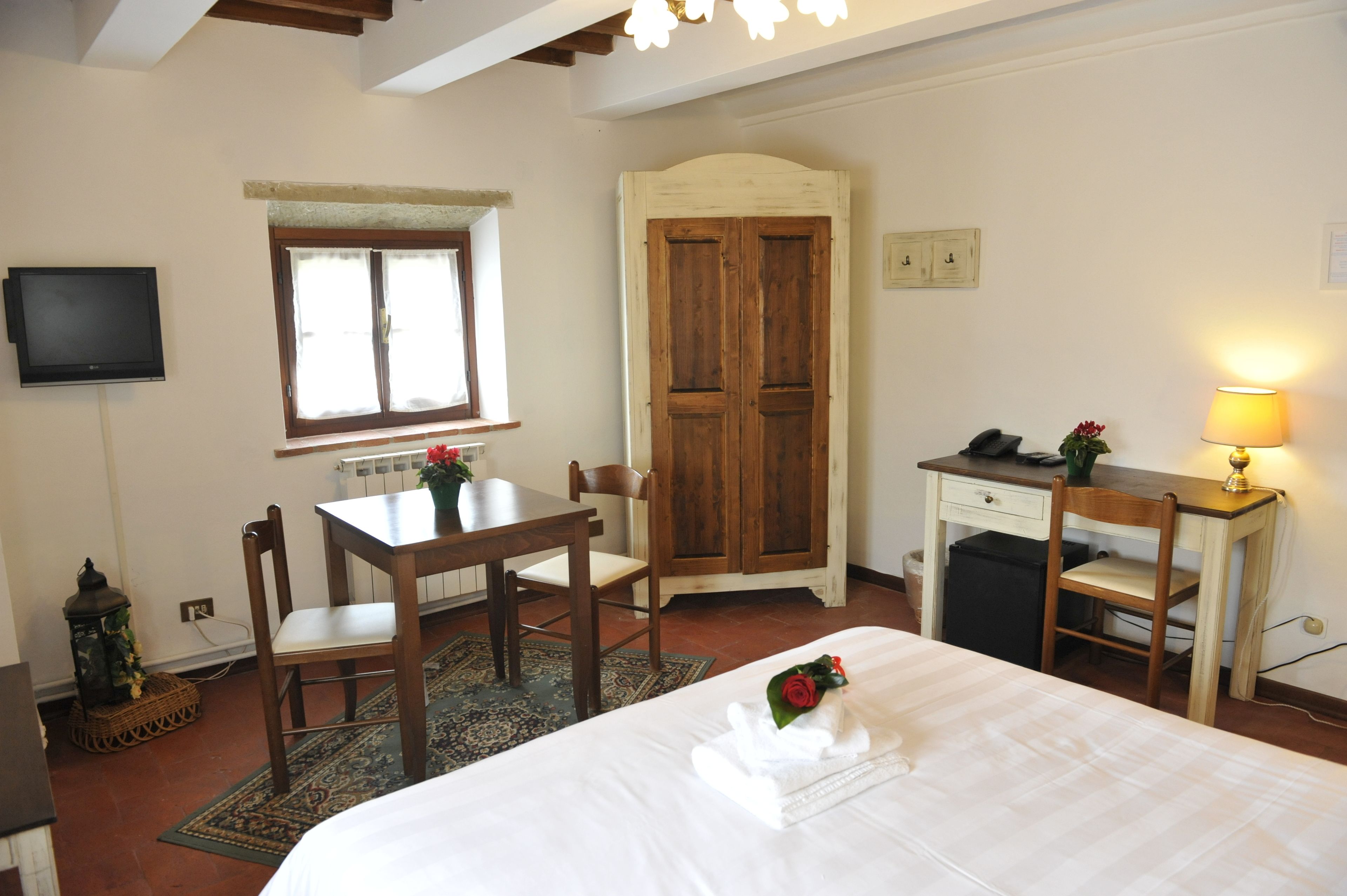A hotel room with a bed, a desk, a chair, a wooden wardrobe, a television, and a window with a view.