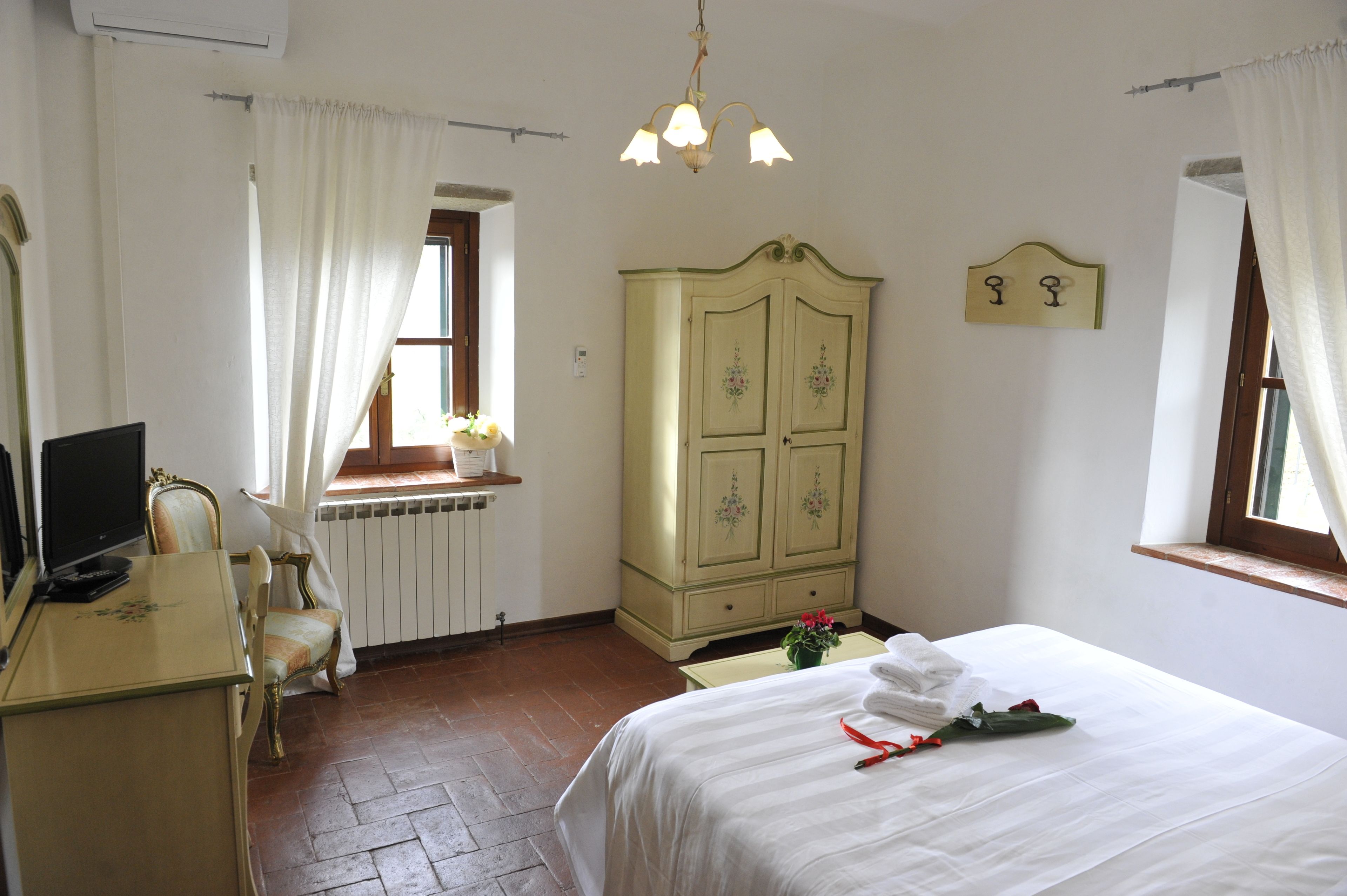 A hotel room with a bed, a desk with a chair, a wardrobe, a window with curtains, and a ceiling light.