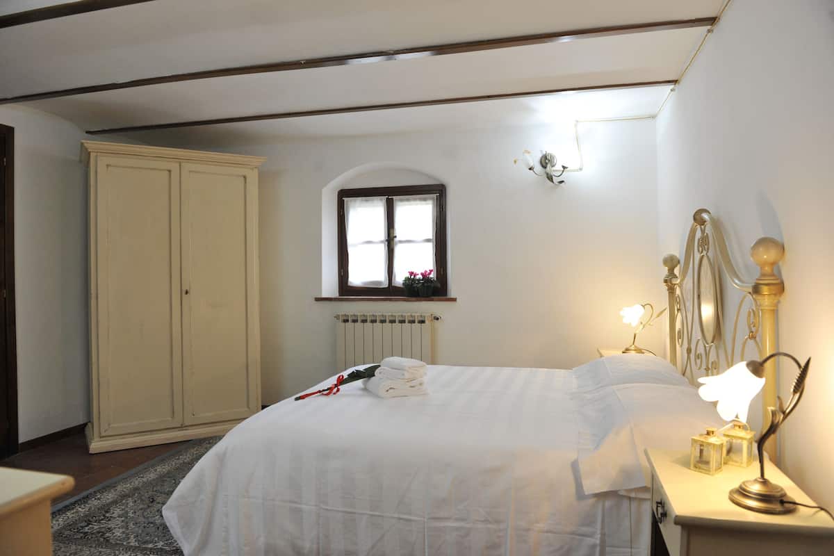Une chambre à coucher avec un lit, une table de chevet avec une lampe, une fenêtre et un radiateur.